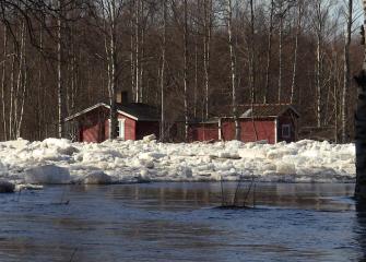 Kevättulva nostaa joen vedenpintaa ja kasaa jäälohkareita rantamökkien edustalle.
