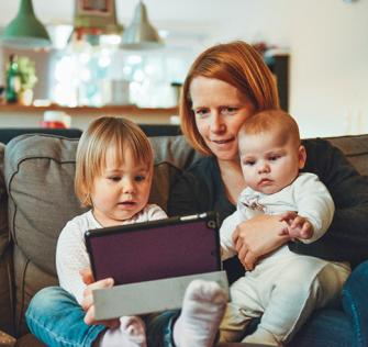 Nainen istuu sohvalla kahden pienen lapsen kanssa sisätiloissa.