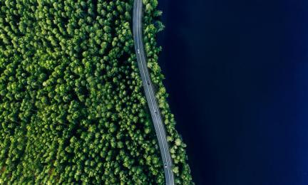 Ilmakuva tiestä vihreän metsän ja sinisen järven välissä Suomessa.